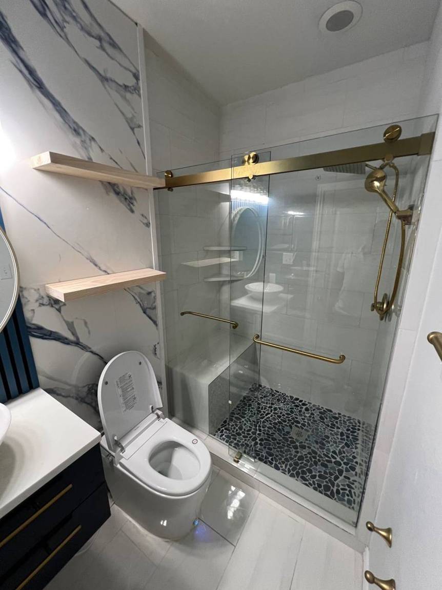 Extended shower with tiled bench, pebble floor and gold sliding glass door