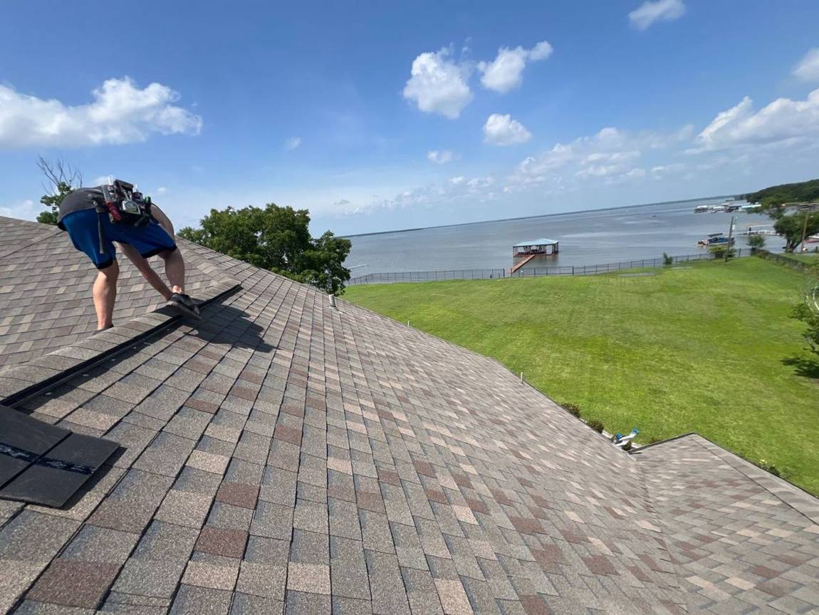 Roofer installing ridge vent on a new shingle roof overlooking Lewisville Lake
